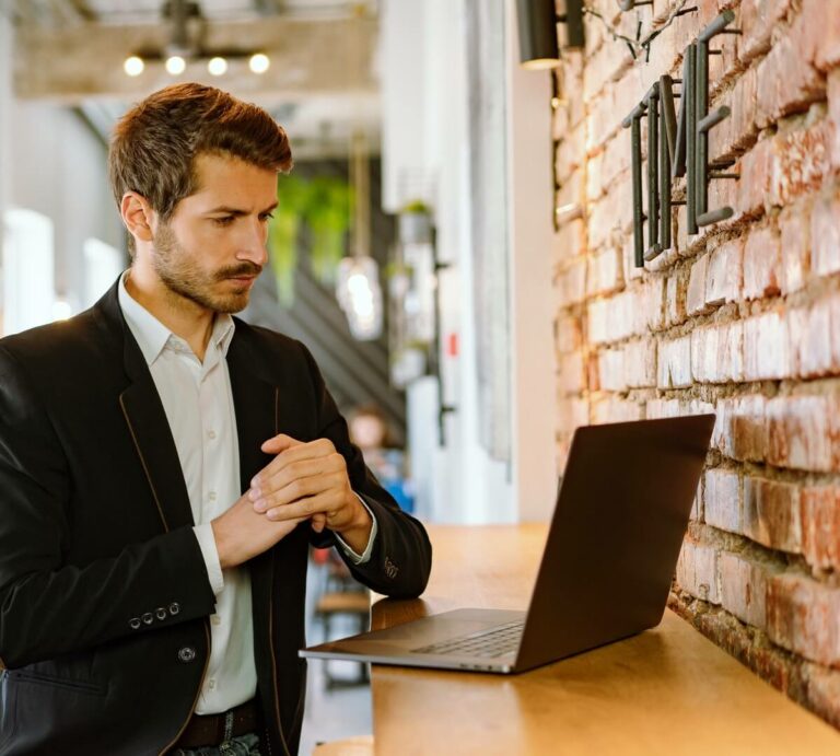 man in suit jacket standing at a counter in front of a laptop